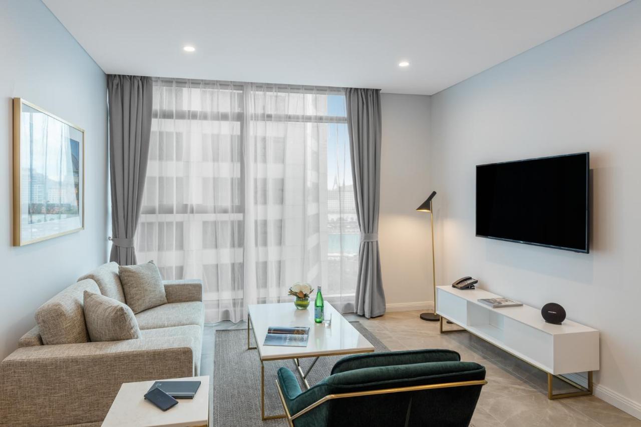 Meriton Suites Sussex Street, Sydney Eksteriør billede The photo shows a modern living room space with a light, airy ambiance. It features a comfortable beige sofa with decorative cushions, a sleek coffee table placed in front, and a dark green armchair. There is a large window covered with sheer curtain