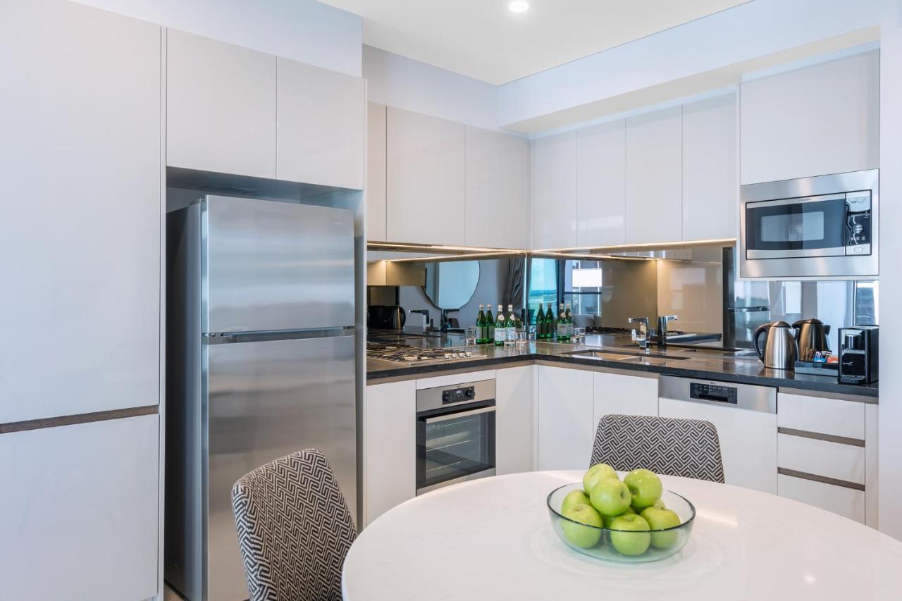 Meriton Suites Sussex Street, Sydney Eksteriør billede The photo displays a modern kitchen with a sleek design. It features light-colored cabinetry and a countertop with a polished finish. On the left, there is a stainless steel refrigerator. The kitchen is equipped with various appliances, including an 