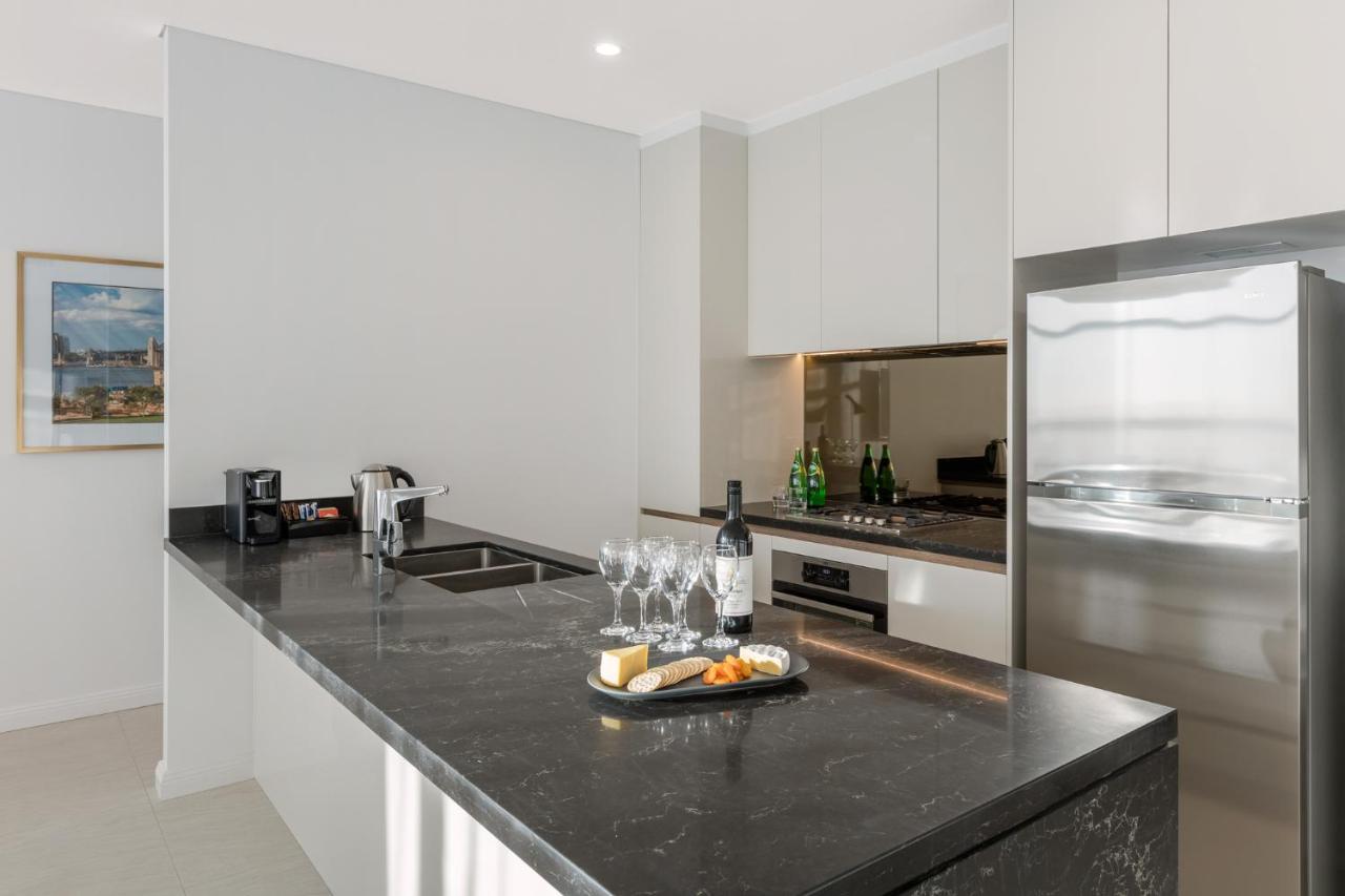 Meriton Suites Sussex Street, Sydney Eksteriør billede The photo shows a modern kitchen featuring a sleek design with a dark stone countertop. There is a built-in sink and possibly a cooktop. The kitchen cabinetry is light-colored, creating a contrast with the dark counter. On the countertop, there are w