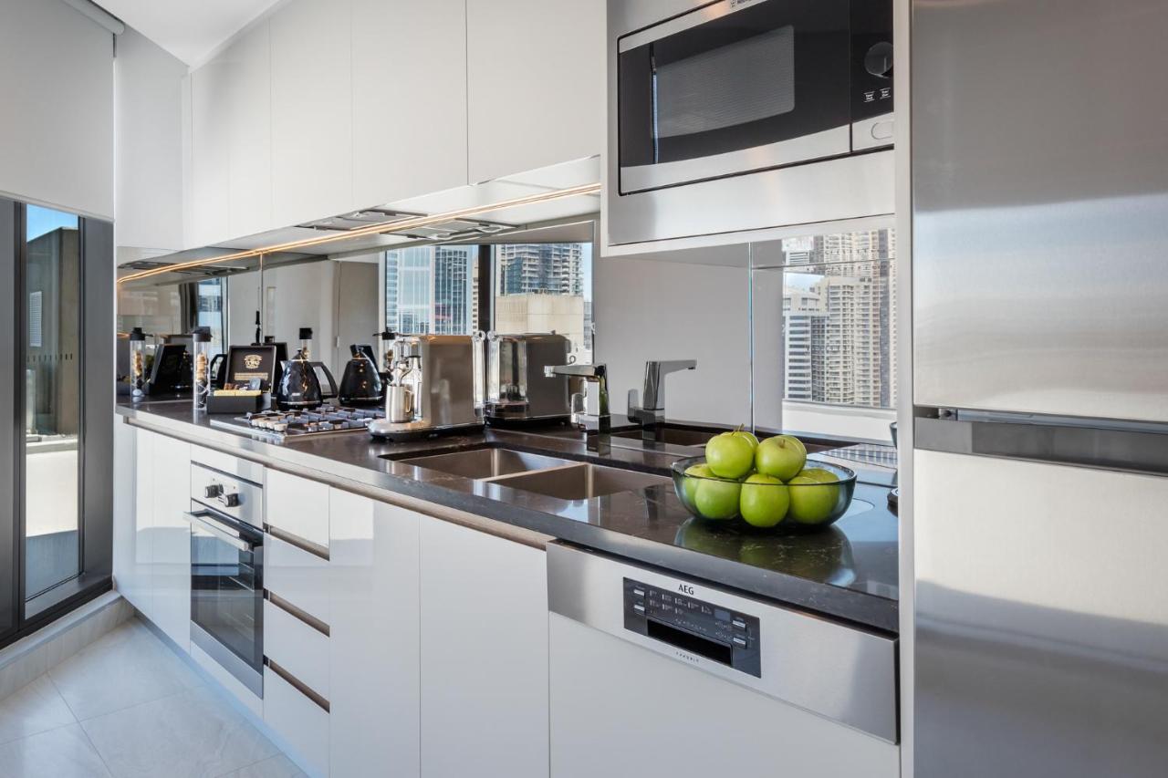 Meriton Suites Sussex Street, Sydney Eksteriør billede The photo shows a modern kitchen featuring sleek cabinetry and stainless steel appliances. There is a glossy countertop with a bowl of green apples as a decoration. The kitchen includes a built-in oven, a microwave, and other kitchen gadgets, along w