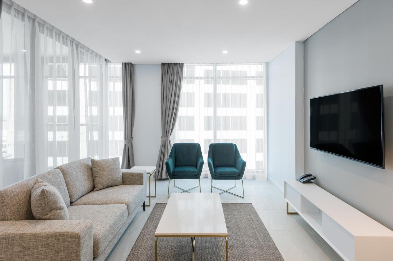 Meriton Suites Sussex Street, Sydney Eksteriør billede The photo shows a modern living room equipped with a light gray sofa, two teal chairs, and a coffee table in the center. The room features large windows with sheer curtains, allowing natural light to illuminate the space. There is a white media conso