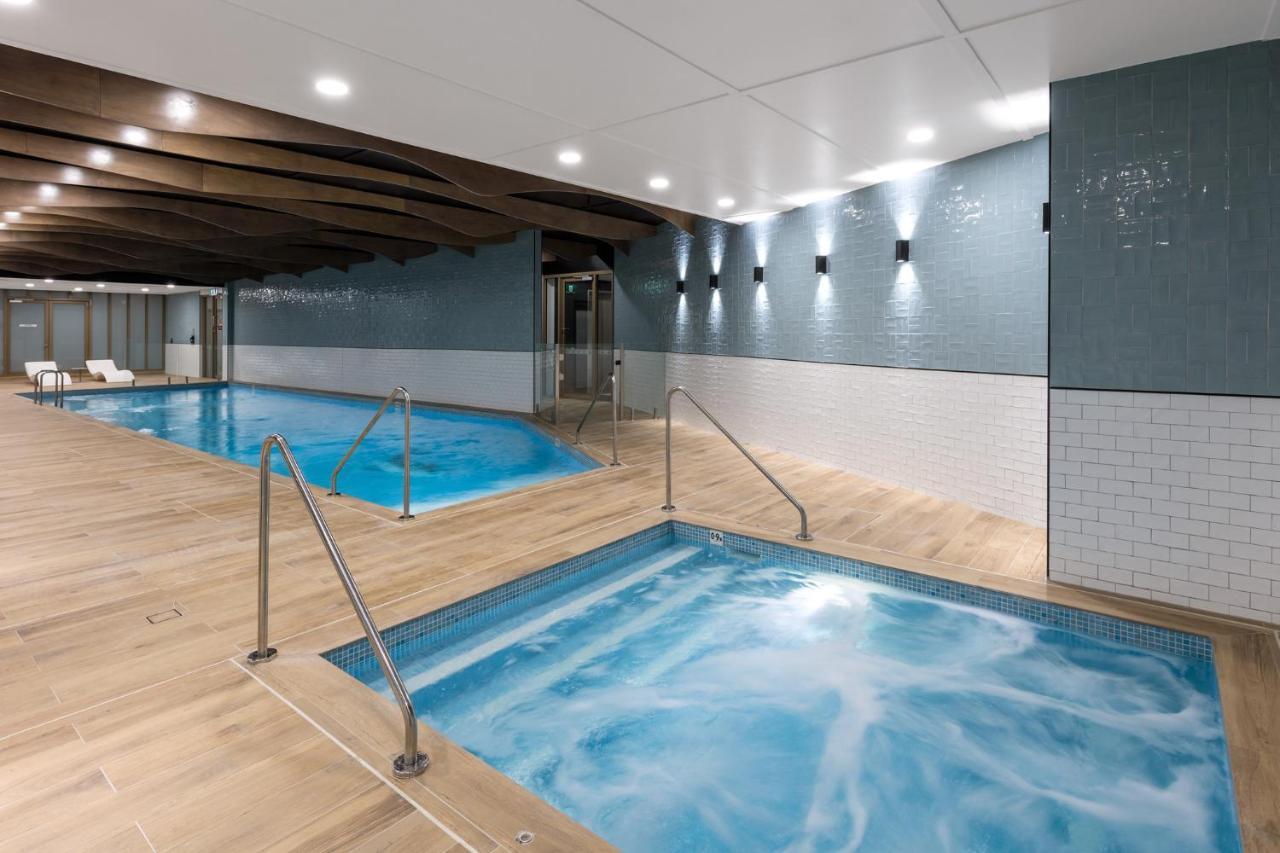 Meriton Suites Sussex Street, Sydney Eksteriør billede The photo shows a modern indoor spa area. There are two pools: one is larger and has a clear blue water, while the other is smaller, possibly a hot tub, with jets creating bubbles. The walls are a mix of blue tiles and white tiles, and the floor is m