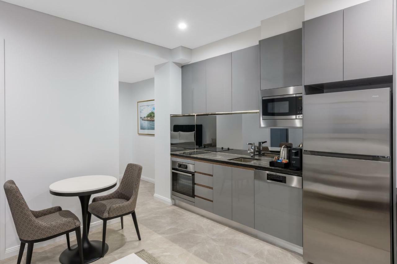 Meriton Suites Sussex Street, Sydney Eksteriør billede The photo shows a modern kitchen area that features a sleek design. The cabinetry and appliances are in shades of gray, giving it a contemporary look. There is a stainless steel refrigerator, microwave, and oven, along with a sink and cooking area. 
